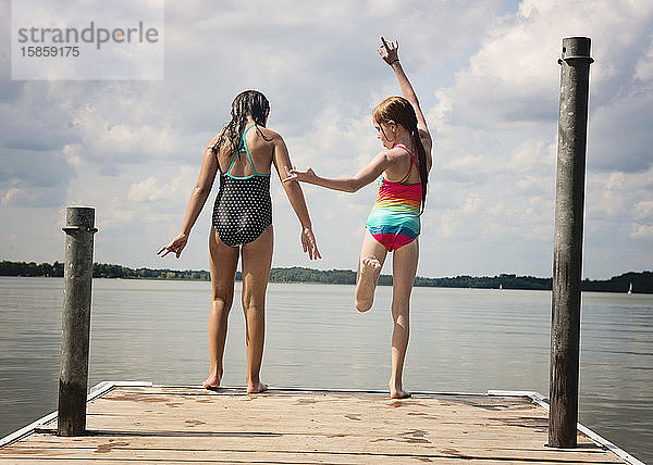 Zwei junge Mädchen in Badeanzügen wollen von einem Dock in einen See springen