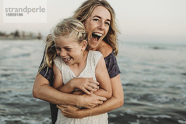 Mutter umarmt junges Mädchen mit Sommersprossen im Meer lachend
