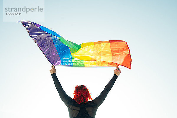 Frau hält die schwule Regenbogenfahne auf blauem Himmelshintergrund. Glück  Freiheit und Liebeskonzept für gleichgeschlechtliche Paare.