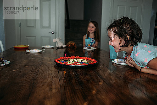 Seitenansicht eines Mädchens  das an ihrem Geburtstagskuchen lächelnd an einem Tisch sitzt