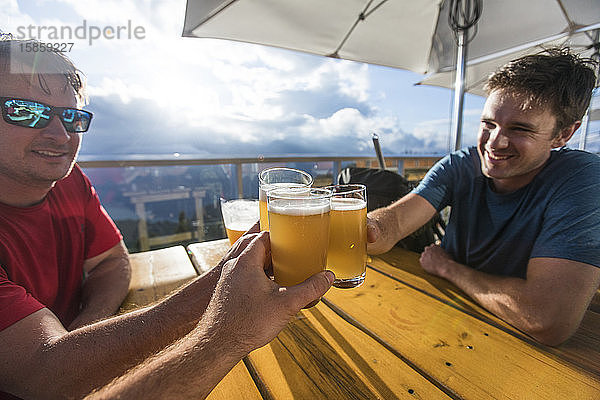 Drei Männer stoßen auf der Restaurant-Terrasse auf ihr Bier an