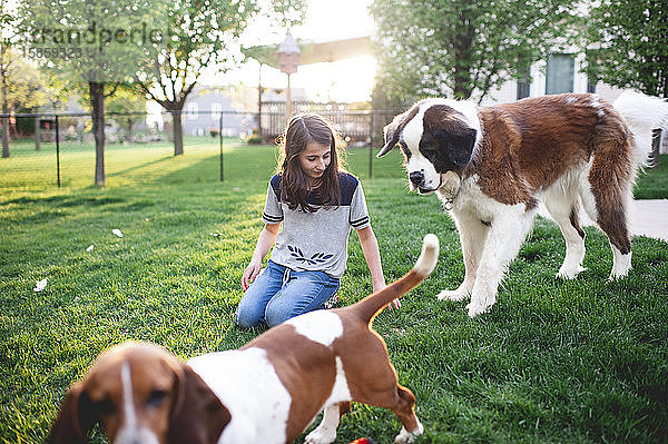 Zwischen Mädchen sitzt im Gras und spielt mit 2 Hunden im heimischen Garten