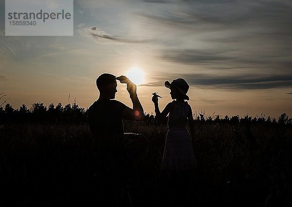 Silhouette eines Vaters und einer Tochter  die draußen mit einem Papierflugzeug spielen