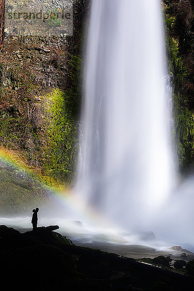 Silhouette einer Person an einem Wasserfall mit einem Regenbogen