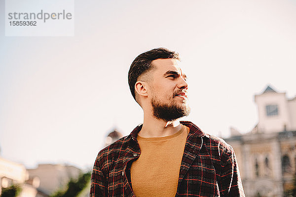 Porträt eines selbstbewussten jungen Hipster-Mannes vor klarem Himmel in der Stadt