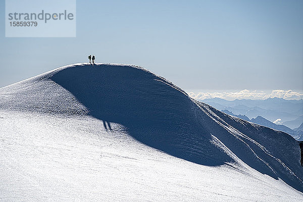 Zwei Bergsteiger stehen als Silhouette auf dem Kamm eines Gletschers auf dem Mt. Baker