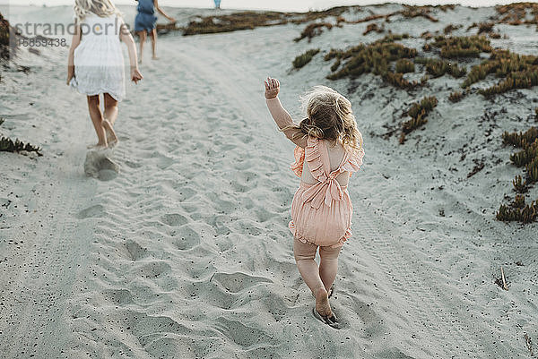 Junges Kleinkind jagt große Schwestern am Strand bei Sonnenuntergang