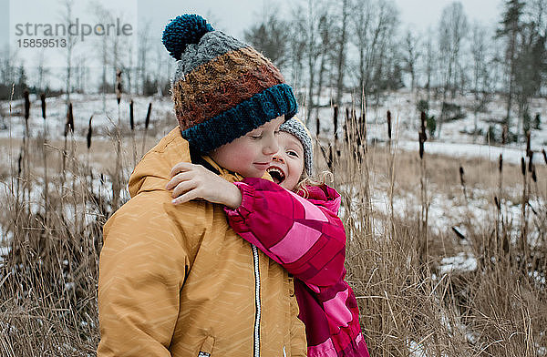 Geschwister  die draussen spielen und kuscheln  während sie im Schnee spielen