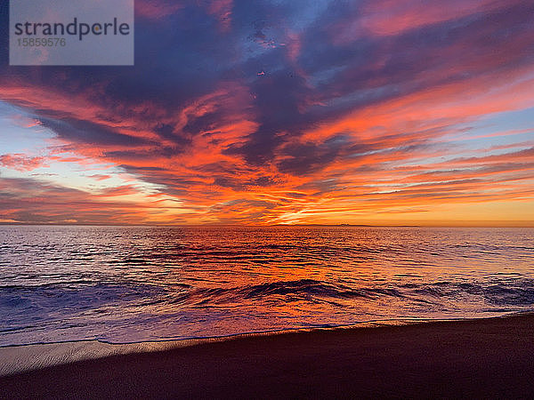 Zuschauerperspektive eines wunderschönen Sonnenuntergangs am Meer  der von Wolken reflektiert wird