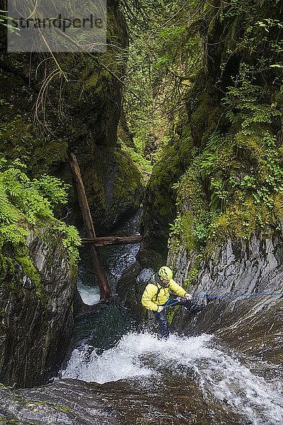 Hochwinkelaufnahme eines Mannes  der sich neben einem Wasserfall im Canyon abseilt.