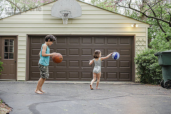 zwei kleine barfüßige Kinder dribbeln Basketbälle in einer Einfahrt