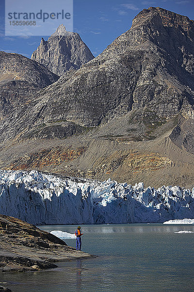 Mann  der am Ufer eines Fjords in Grönland steht