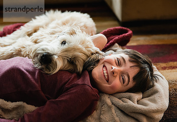 Junge und sein Hund kuscheln sich auf dem Boden auf einer Decke zusammen.