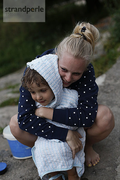 Eine junge erwachsene Frau umarmt einen kleinen Jungen nach dem Schwimmen