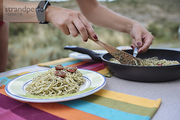 Nahaufnahme von Frauenhänden bei der Zubereitung von Pasta mit Pesto während einer Reise.