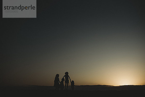 Silhouette von vier jungen Schwestern am Strand bei Sonnenuntergang