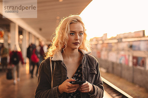Junge Frau hält Smartphone in der Hand  während sie auf den Zug wartet