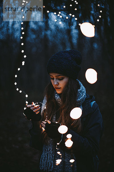 Junge Hipster-Frau hält im Park stehend Weihnachtsbeleuchtung