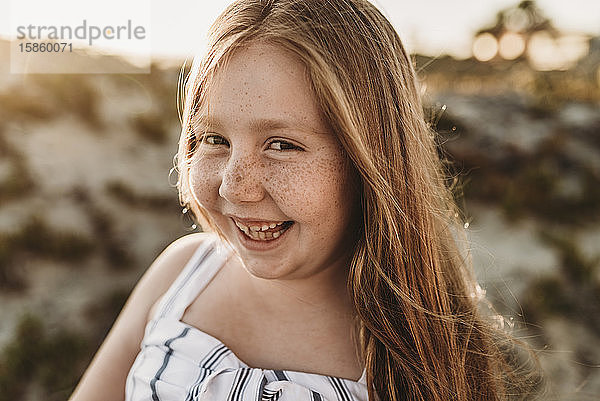 Porträt eines jungen lächelnden rothaarigen Mädchens mit Sommersprossen bei Sonnenuntergang am Strand