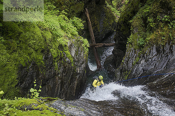 Hochwinkelaufnahme eines Mannes  der sich von einem Wasserfall abseilt.