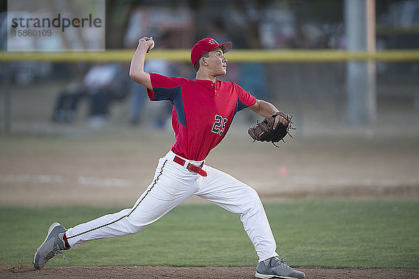 jugendlicher Baseballspieler Pitcher in roter Uniform in voller Windstärke auf dem Hügel