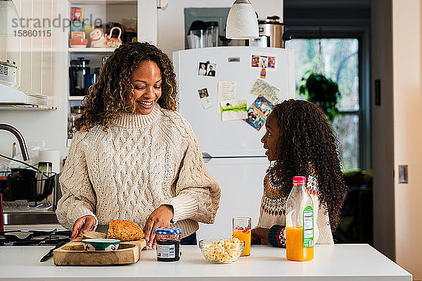 Mädchen im Gespräch mit lächelnder Mutter  die zu Hause in der Küche das Frühstück vorbereitet