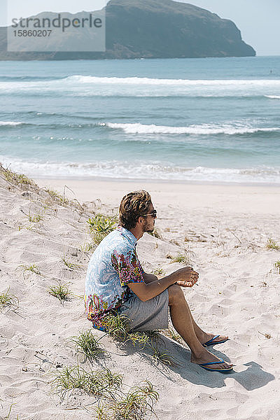 Junger Mann sitzt am Strand