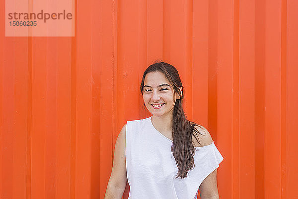 Lächelnde junge Frau lehnt im Freien an einer Wand