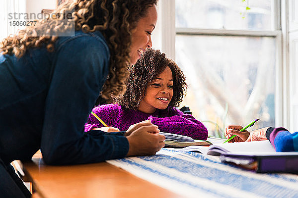 Lächelnde Mutter hilft Töchtern bei den Hausaufgaben zu Hause
