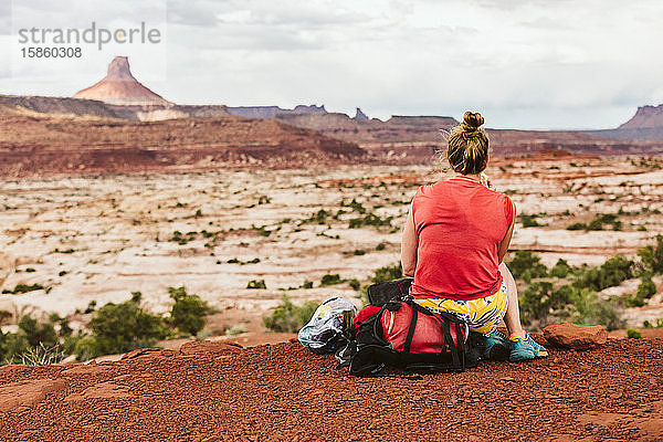 verschwitzte Frau sitzt während einer Wanderpause mit Blick auf die Wüste auf ihrem Rucksack