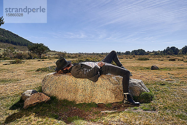 Porträt eines jungen tätowierten Mannes  der auf einem Felsen in der Landschaft liegt