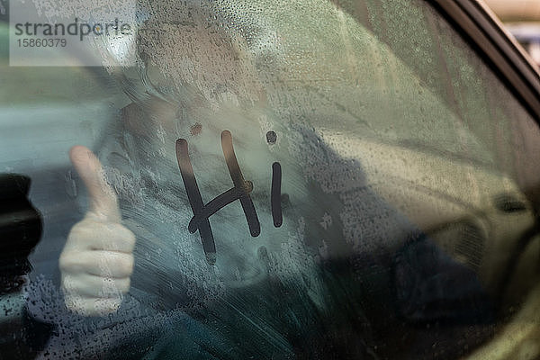 Teenager gibt von innen den Daumen hoch  wenn Auto mit Schriftzug am Fenster