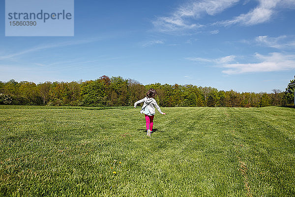 Ein fröhliches kleines Mädchen in heller Kleidung läuft im Frühling durch ein Feld