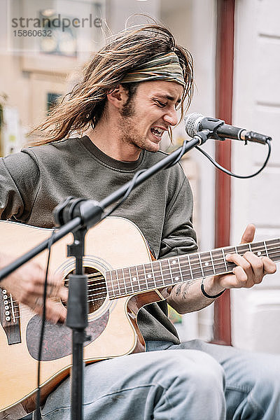 Junger Rocker mit langen Haaren und einem Stirnband  der vor einem Mikrofon Gitarre spielt