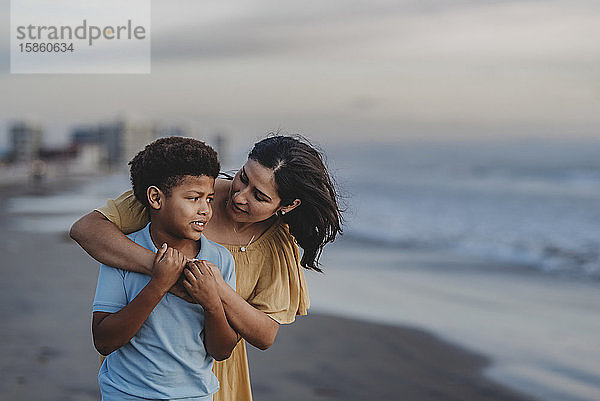 Nahaufnahme einer Mutter  die einen Jungen im Schulalter am Strand umarmt