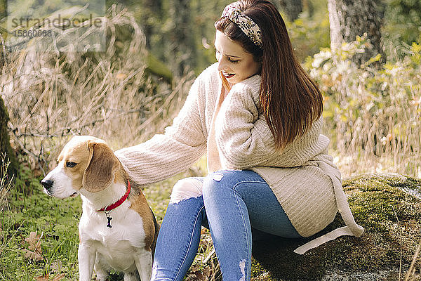 Lächelnde junge Frau  die während eines Spaziergangs neben ihrem Hund sitzt