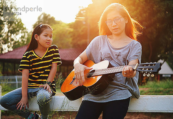 Mutter zeigt ihrer Tochter  wie man Gitarre spielt