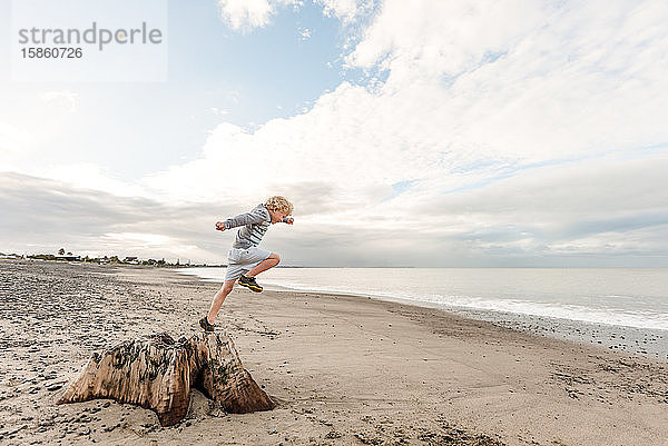 Junge springt am Strand vom Baumstumpf