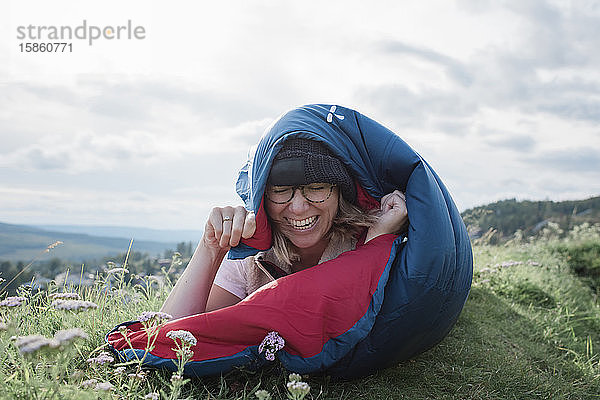 Frau lächelnd und lachend in einem Schlafsack liegend beim Camping in der Natur