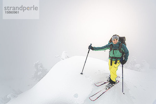 Junge Frau lächelt Backcountry-Skifahren auf schneebedecktem Gipfel in Squamish