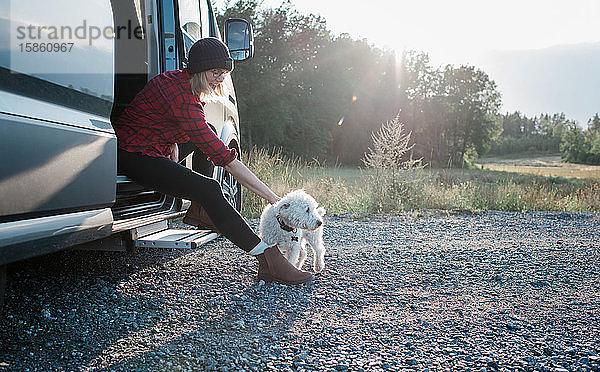 Frau sitzt auf einem Wohnmobil und streichelt beim Camping ihren Hund