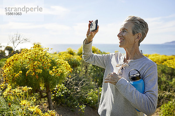 Fröhliche ältere Frau fotografiert durch ein Smartphone  während sie an einem sonnigen Tag am Himmel steht