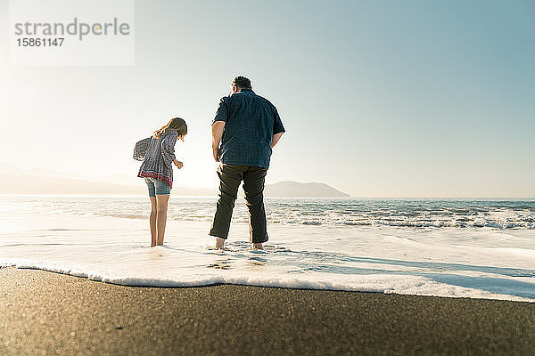 Vater und Tochter stehen bei Sonnenuntergang am Strand im Wasser