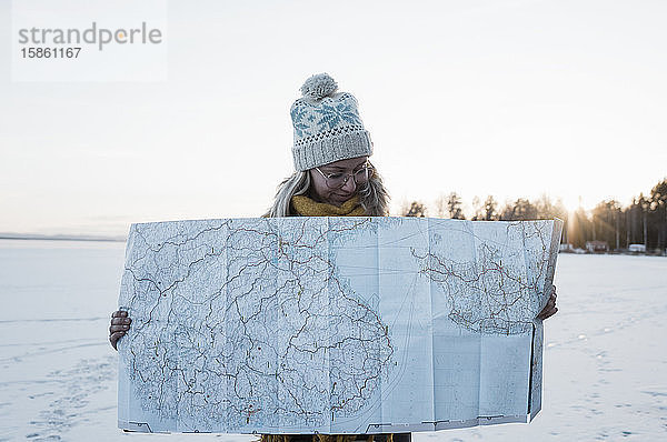 Frau  die eine Karte hochhält  während sie im Winter auf einem gefrorenen See steht