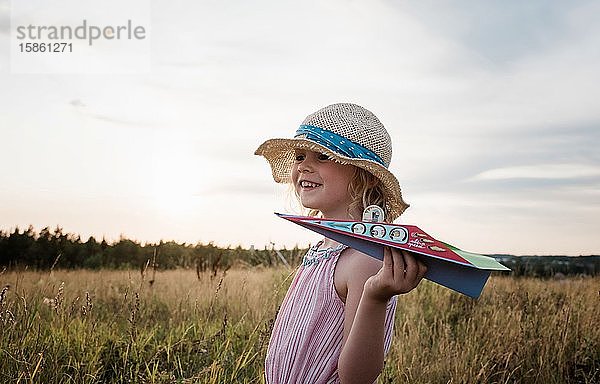 Porträt eines Mädchens  das bei Sonnenuntergang auf einer Wiese mit einem Papierflugzeug spielt