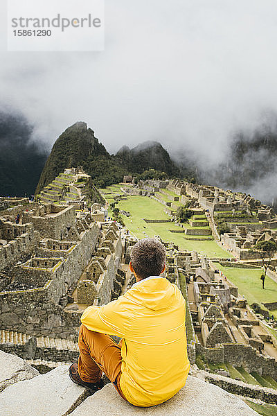 Ein Mann in einer gelben Jacke sitzt in der Nähe der Ruinen von Machu Picchu  Peru