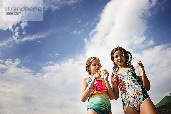 Zwei junge Mädchen in Badeanzügen mit gefrorenen Leckereien gegen den blauen Himmel