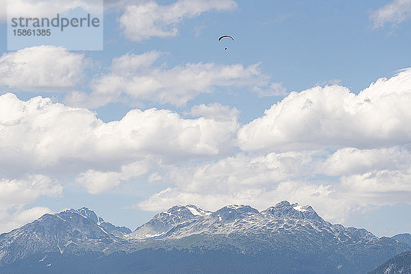 Gleitschirmflieger fliegen an einem sonnigen Tag hoch über schneebedeckten Bergen.