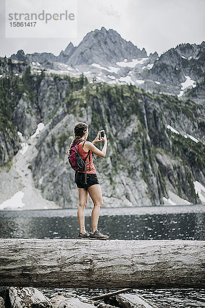 Eine Wanderin macht beim Wandern entlang eines Sees ein Zellenfoto