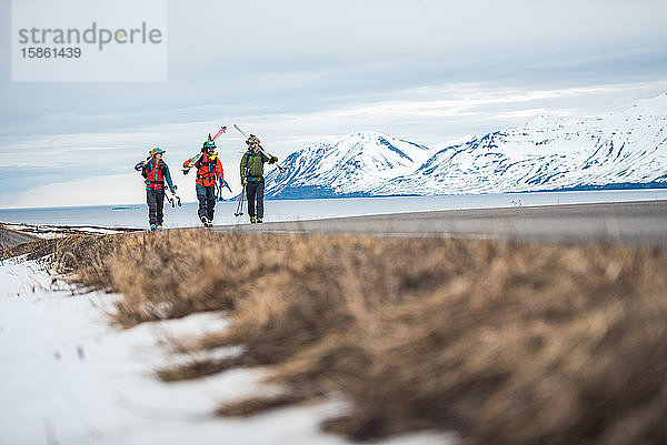 Drei Personen gehen auf einer gepflasterten Straße mit Bergen und dem Meer dahinter